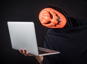A creepy man in a pumpkin halloween mask stands holding a computer, scamming your self-directed IRA - BLOG